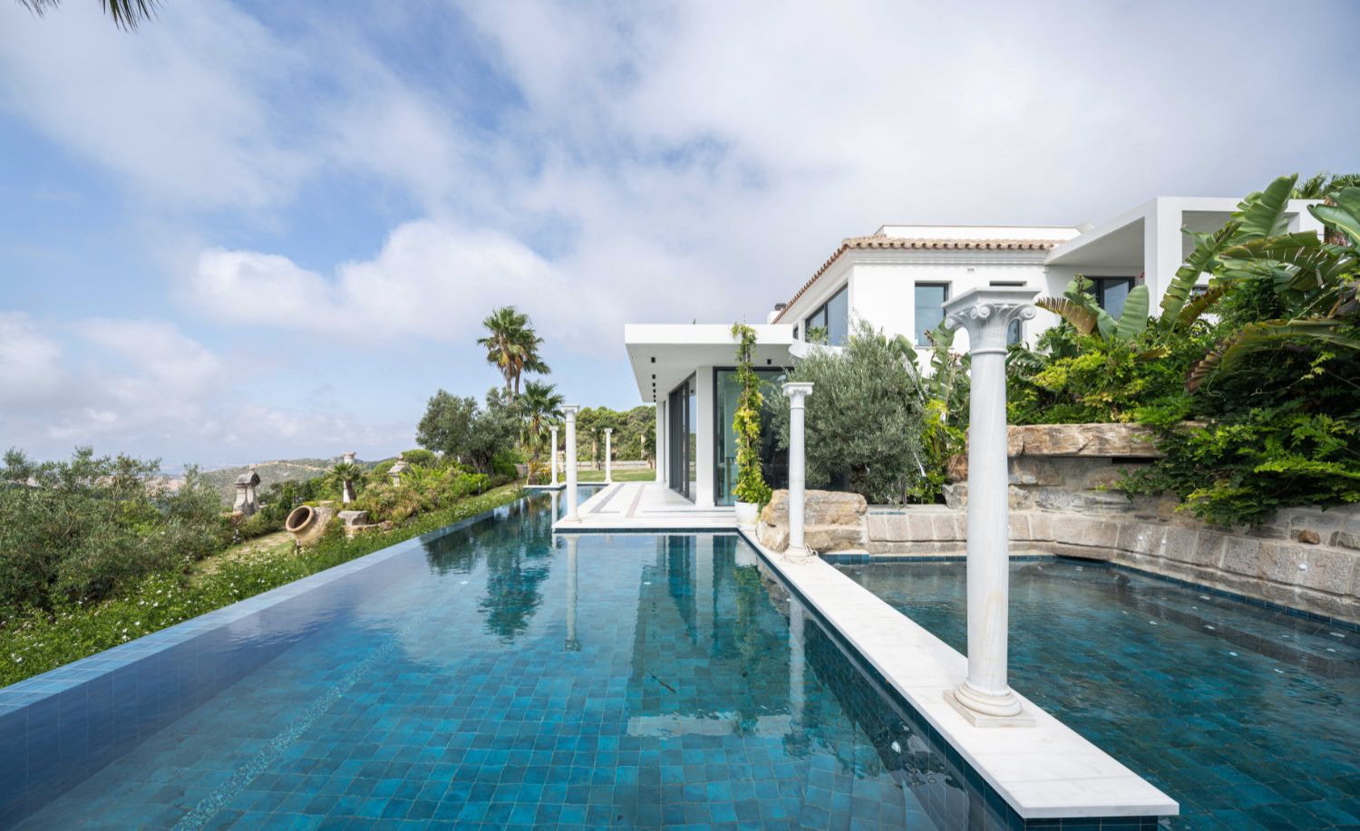 Piscina infinita con columnas de piedra y jardín mediterráneo en la Villa Heritage