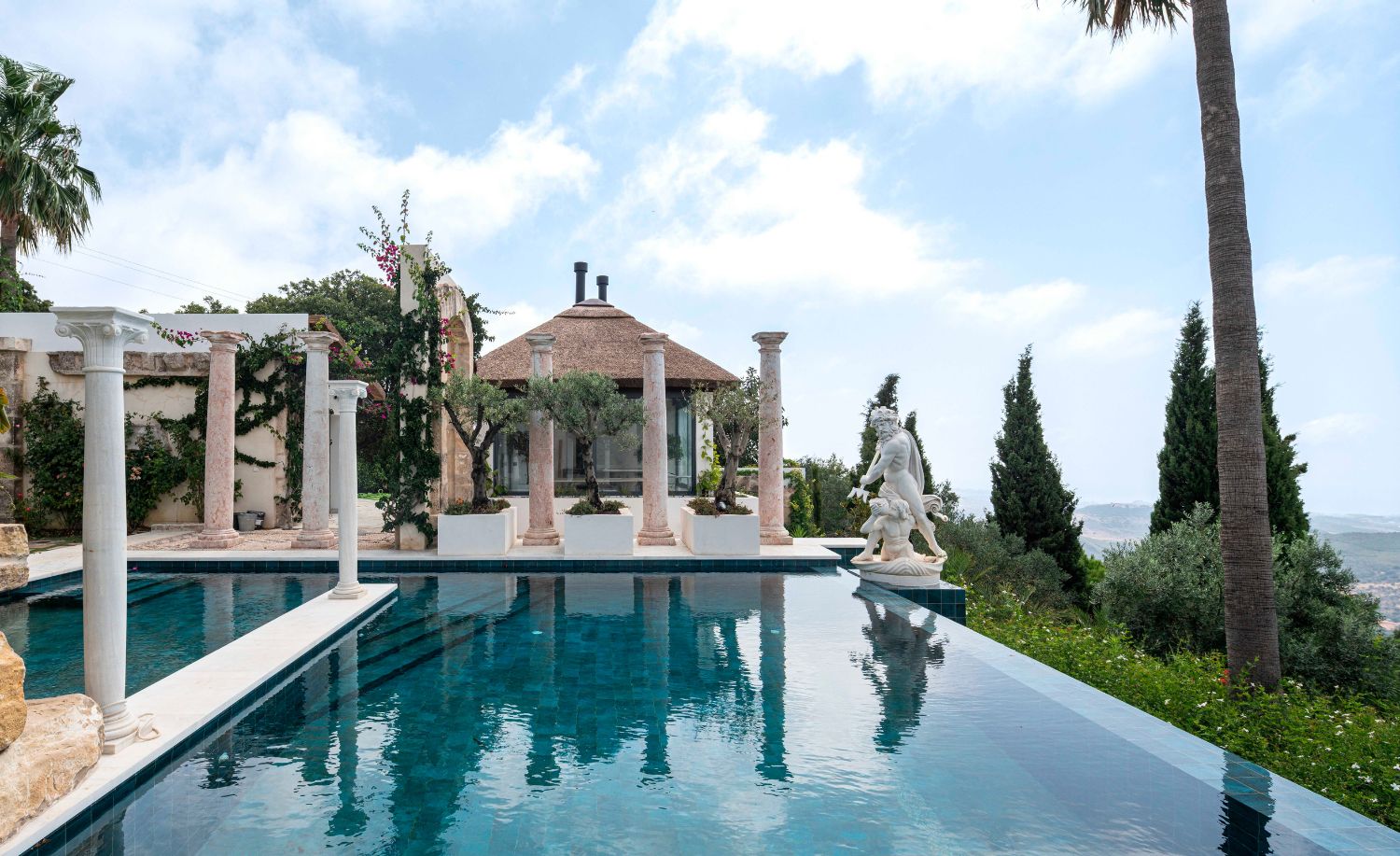 Piscina con pérgola de columnas, escultura y pabellón al fondo en la Villa Heritage