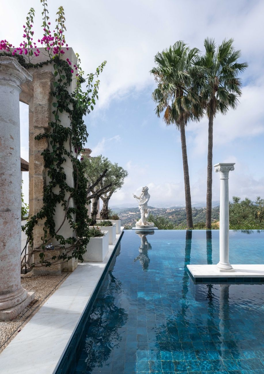 Borde de la piscina infinita con columna antigua y buganvilla en la Villa Heritage