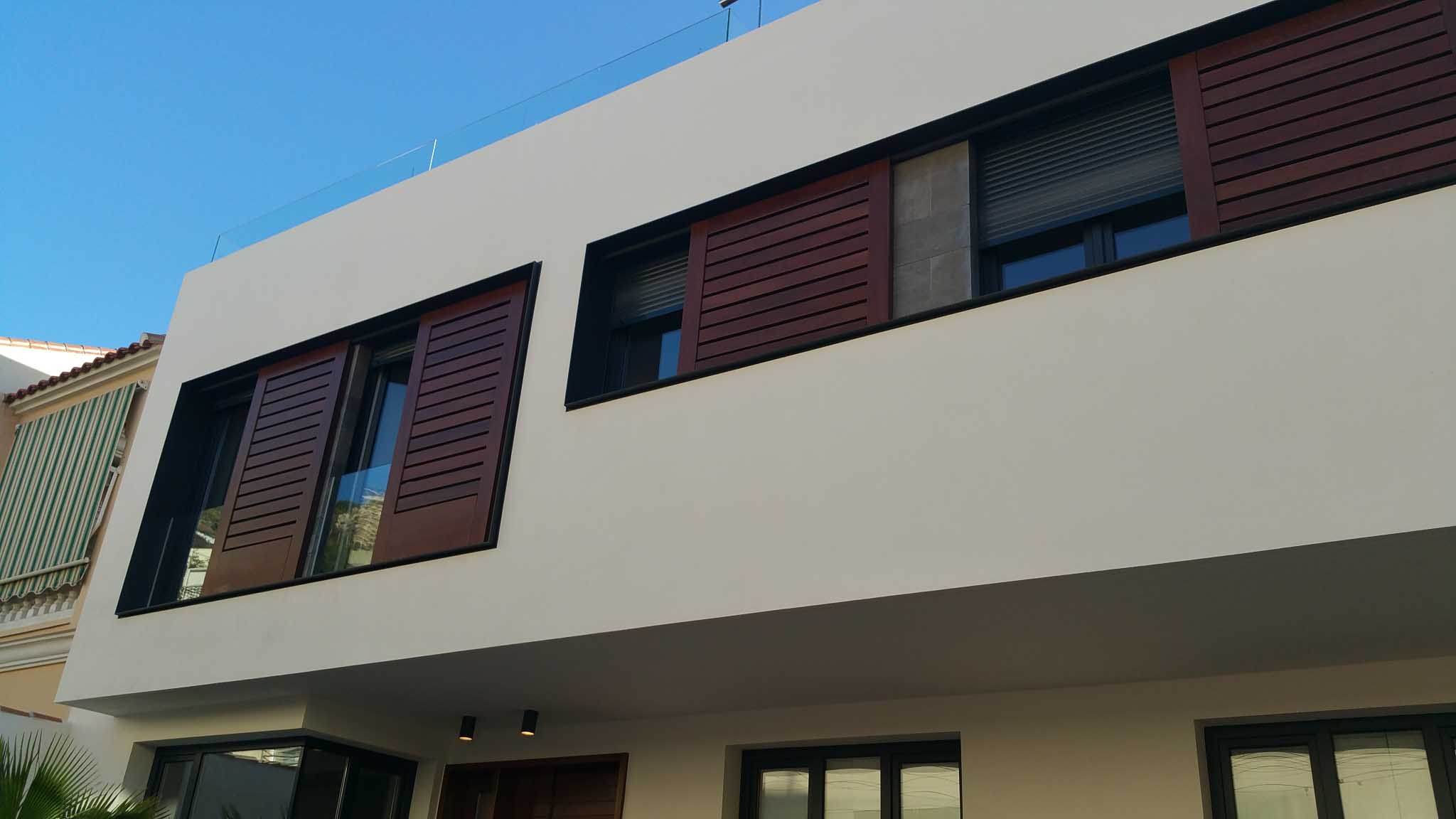 Detalle de la fachada blanca con carpinterías oscuras y lamas de madera en las viviendas de Málaga