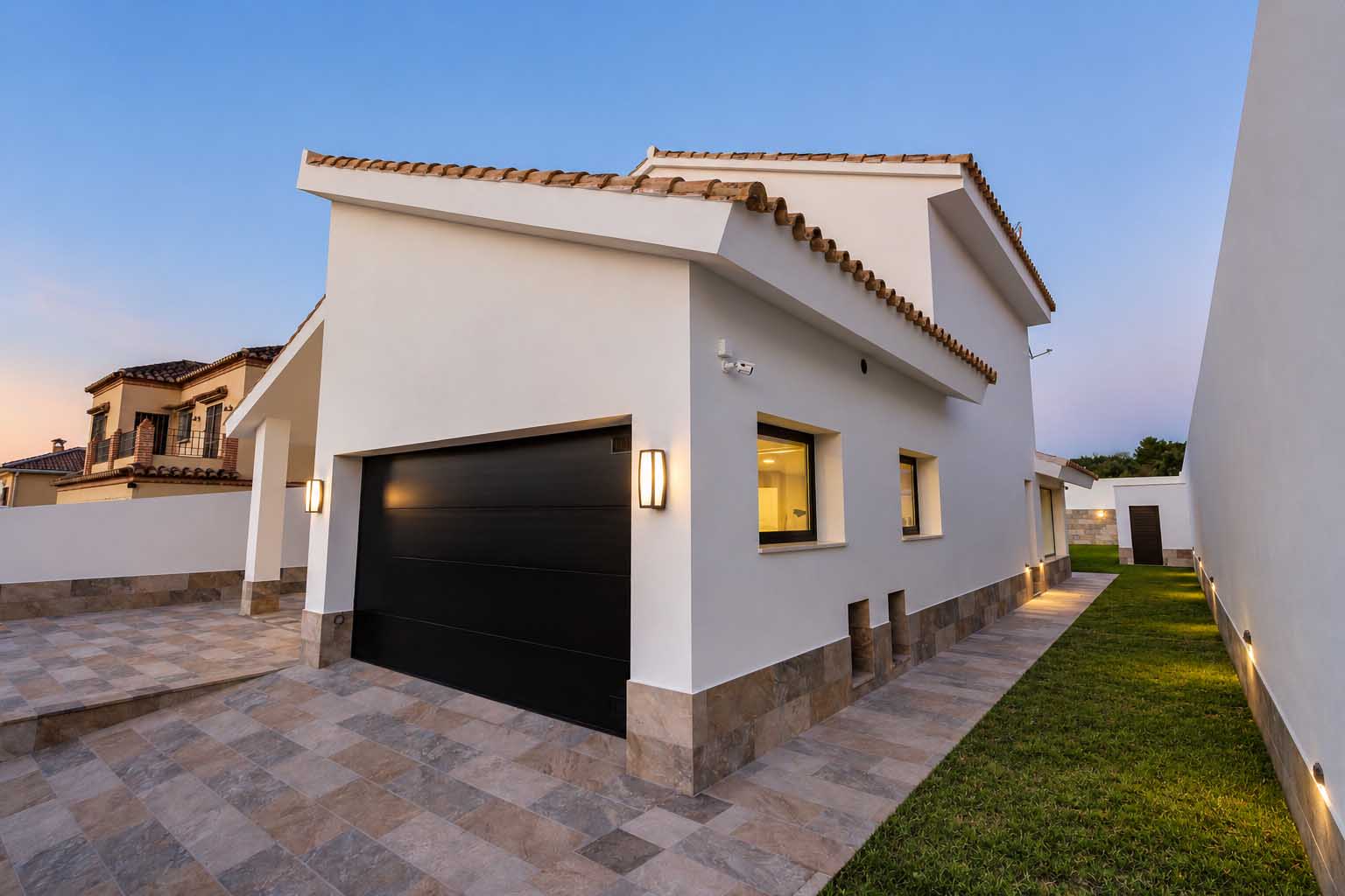 Garaje y fachada blanca con cubierta de teja y jardín lateral con iluminación