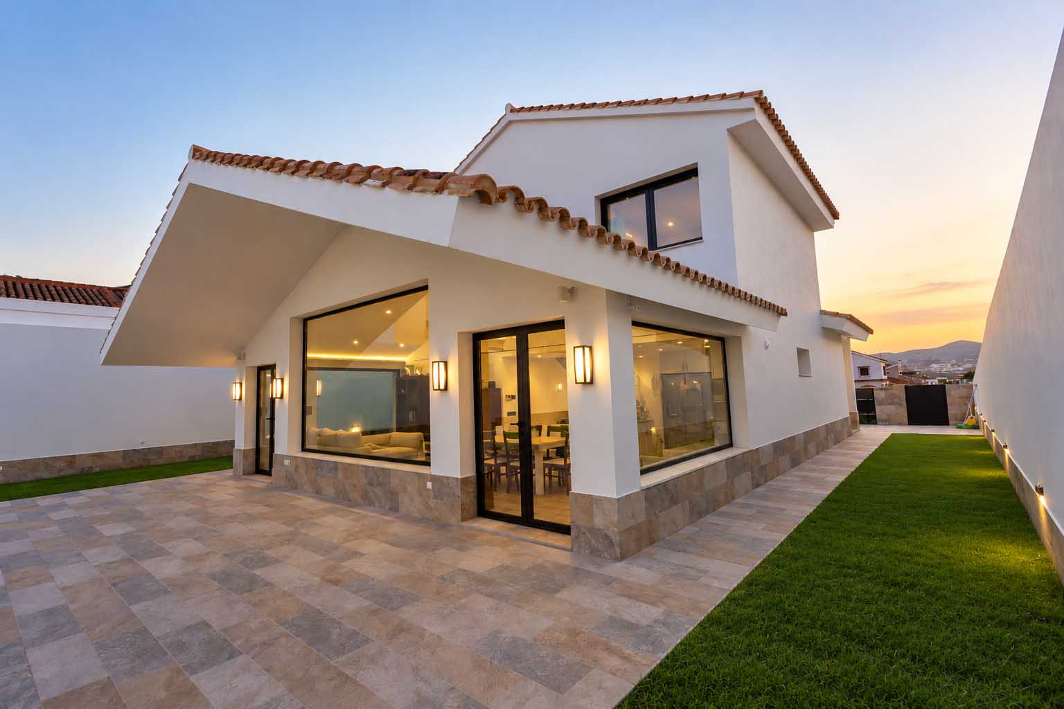 Fachada de la vivienda con cubierta de teja, grandes cristaleras y jardín al atardecer