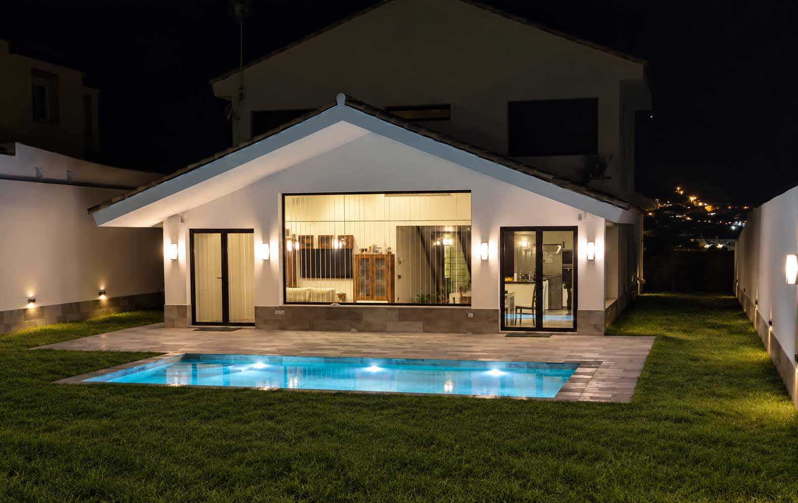 Vivienda con piscina iluminada y jardín de césped de noche