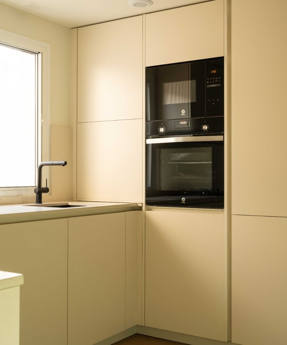 Cocina con muebles blancos y electrodomésticos integrados tras la reforma integral de la vivienda