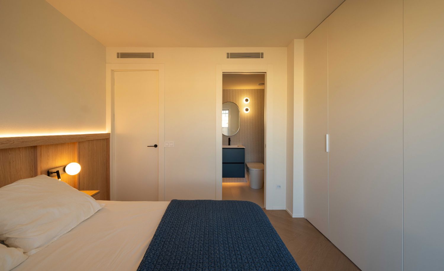 Dormitorio principal con cabecero de madera, iluminación indirecta y baño en suite