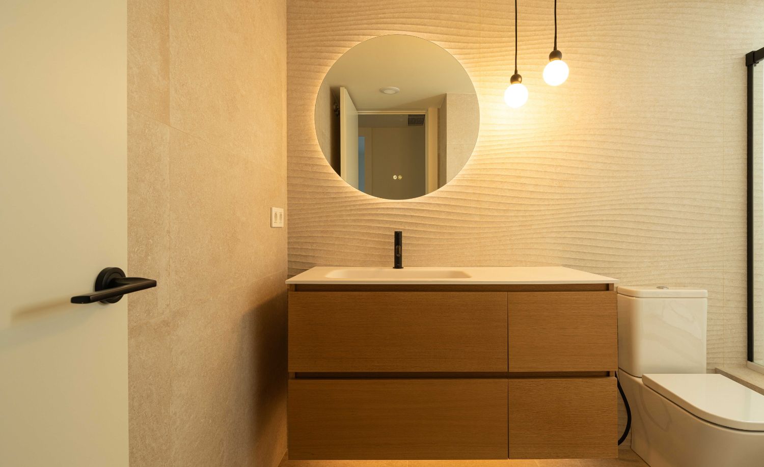 Baño con lavabo sobre mueble de madera, espejo redondo y revestimiento claro