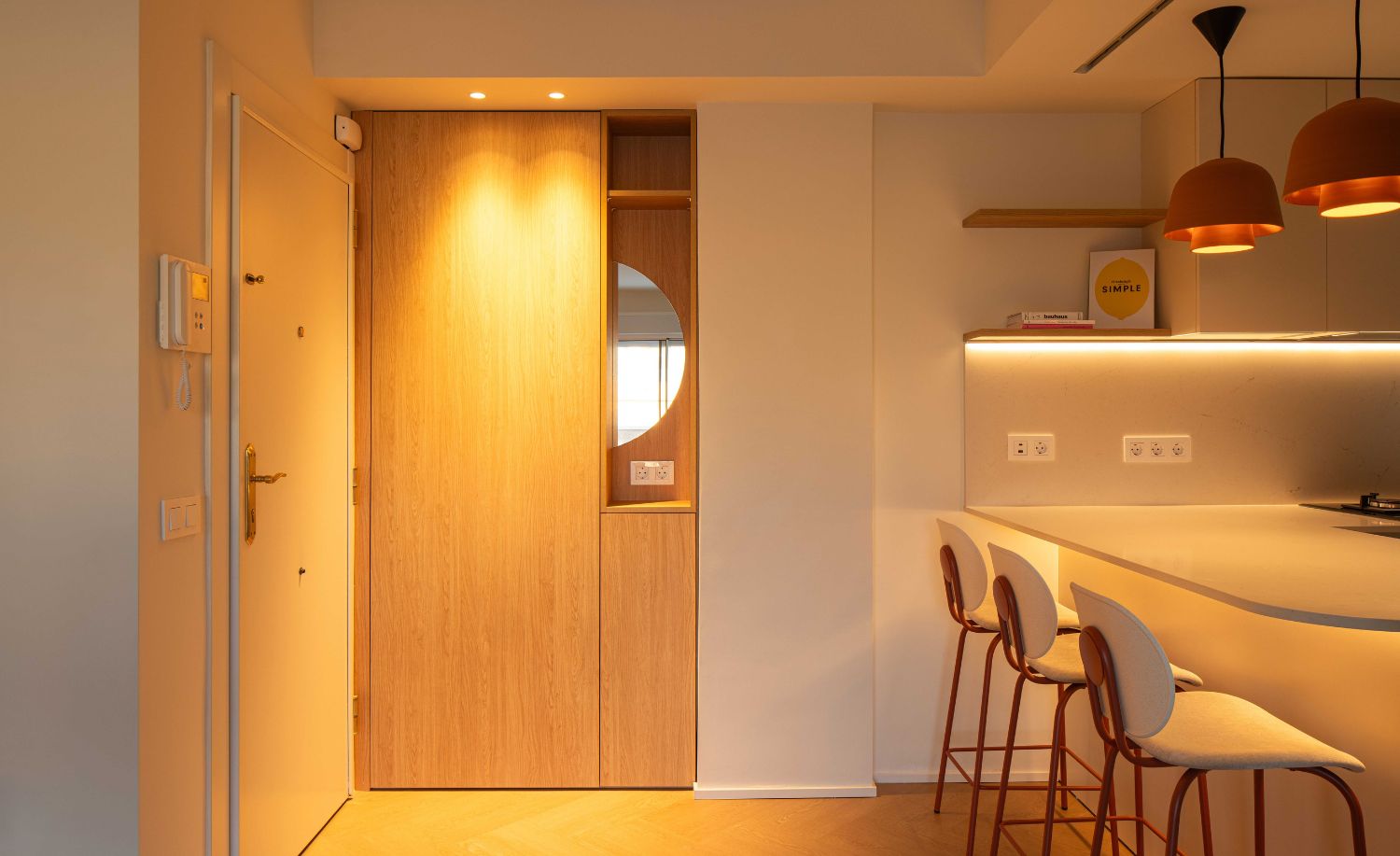 Entrada con armario de madera a medida y cocina abierta con iluminación cálida
