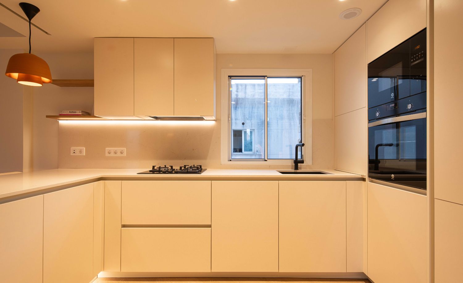 Cocina con encimera clara, horno integrado y luz indirecta bajo los muebles altos