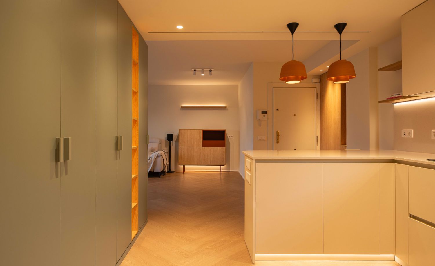 Pasillo con armarios verdes y cocina abierta con iluminación empotrada