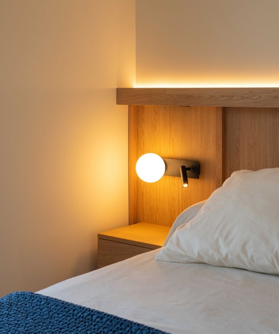 Cama con cabecero de madera y aplique de luz en el dormitorio de la vivienda reformada