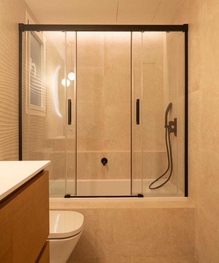 Baño con ducha acristalada de perfilería negra y revestimiento claro