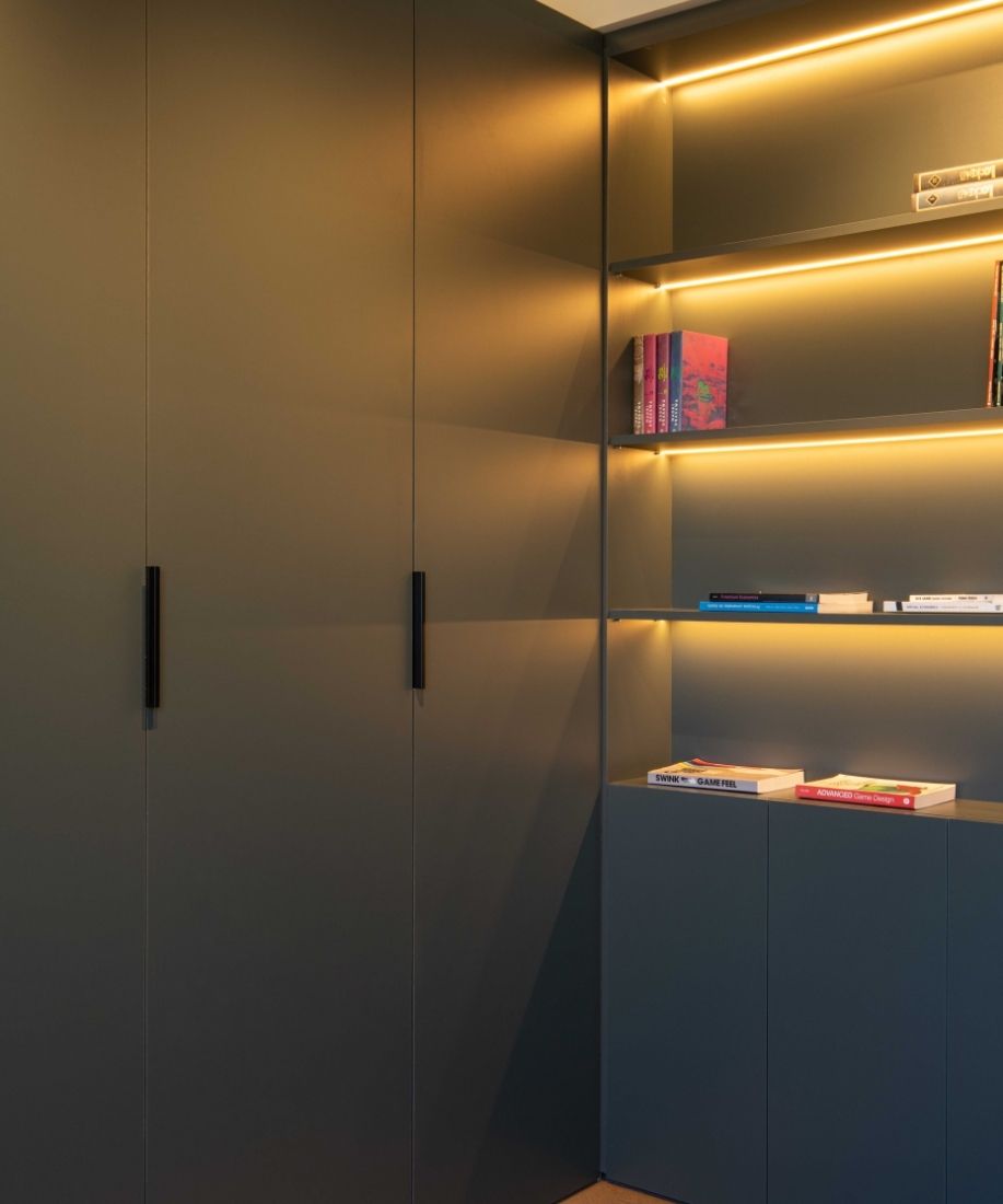 Armario verde oscuro con estanterías iluminadas en la vivienda reformada