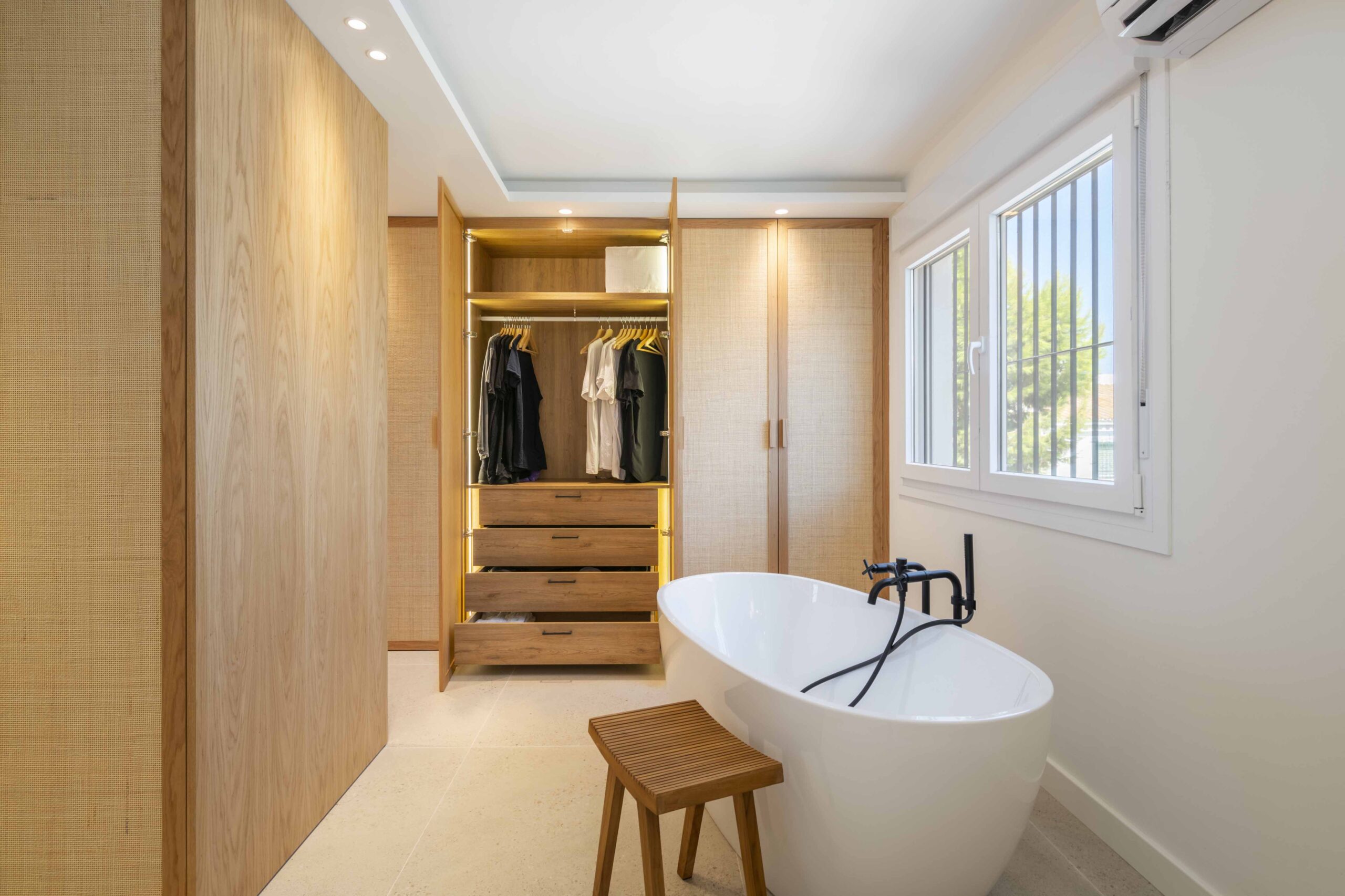 Baño con bañera exenta y vestidor integrado con acabados de fibras naturales