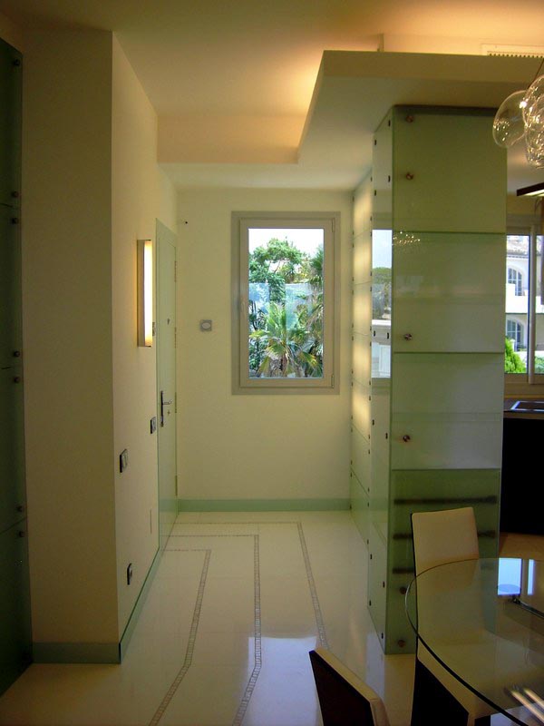 Zona de paso con paneles de vidrio y falso techo retroiluminado en la vivienda de Marbella
