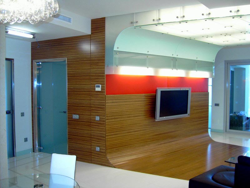 Salón con panel de madera, televisión y falso techo retroiluminado en la reforma de Marbella