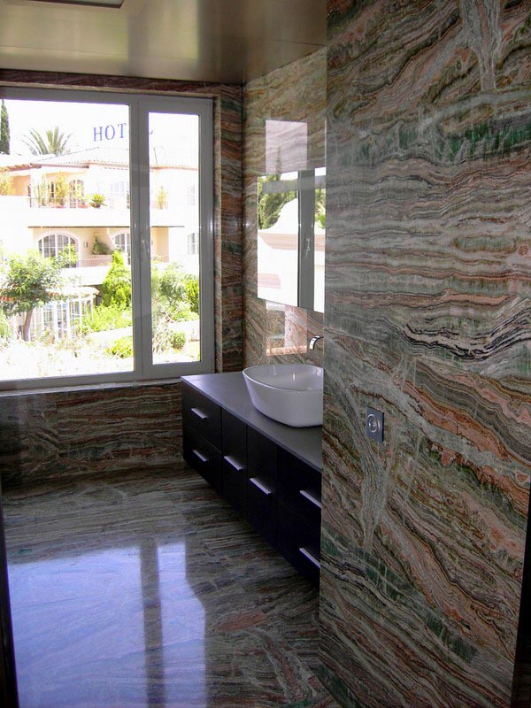 Baño con revestimiento de piedra natural veteada y mueble oscuro en la vivienda de Marbella