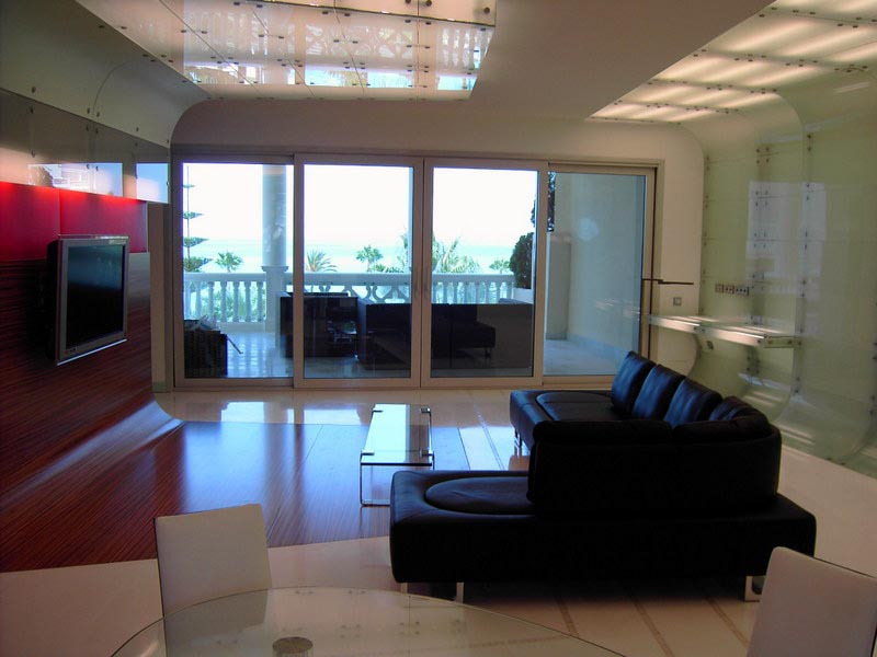 Salón con panel rojo, sofá negro y ventanales con vistas al mar en la vivienda de Marbella
