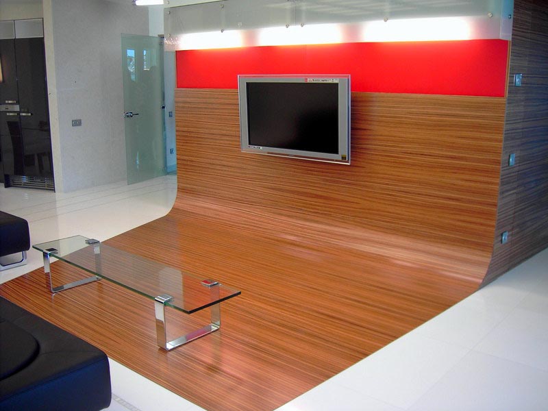 Panel de madera curvo con televisión y mesa de cristal en el salón de la vivienda de Marbella