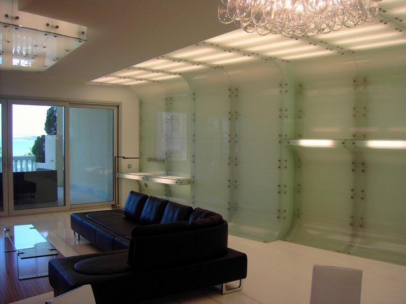 Salón con sofá negro, paredes de vidrio y vistas al mar en la vivienda reformada de Marbella