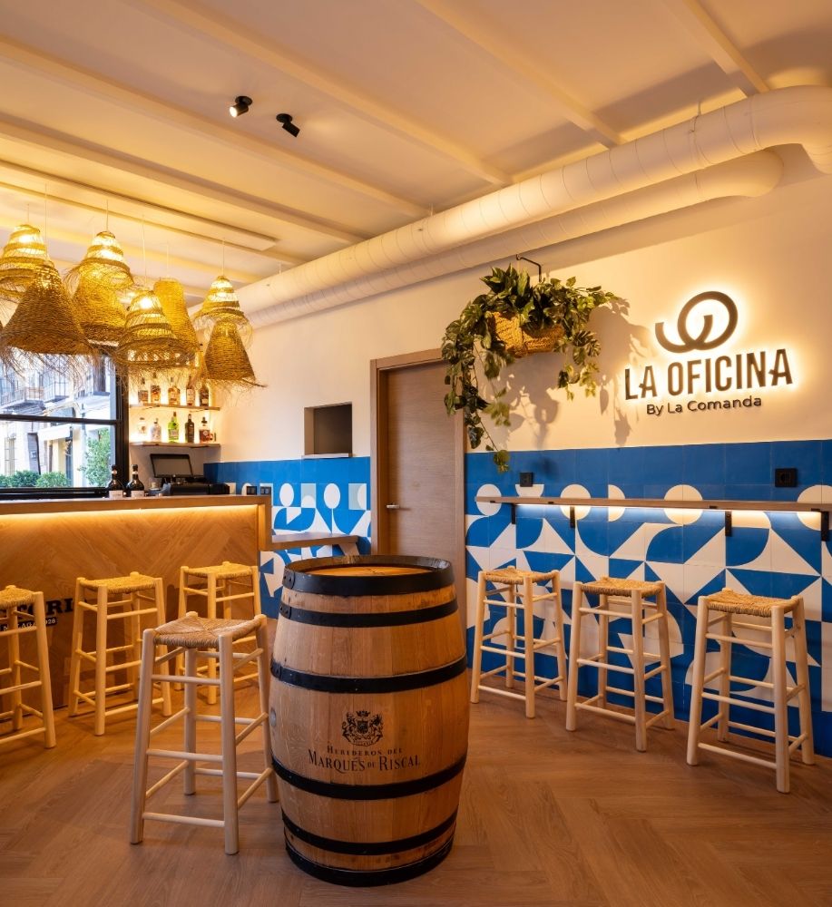 Barra alta con taburetes y barril bajo lámparas de fibra natural en la cervecería La Oficina