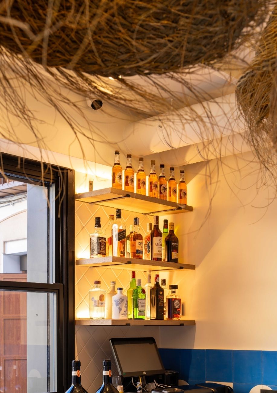 Estantería iluminada con botellas junto a la barra de la cervecería La Oficina