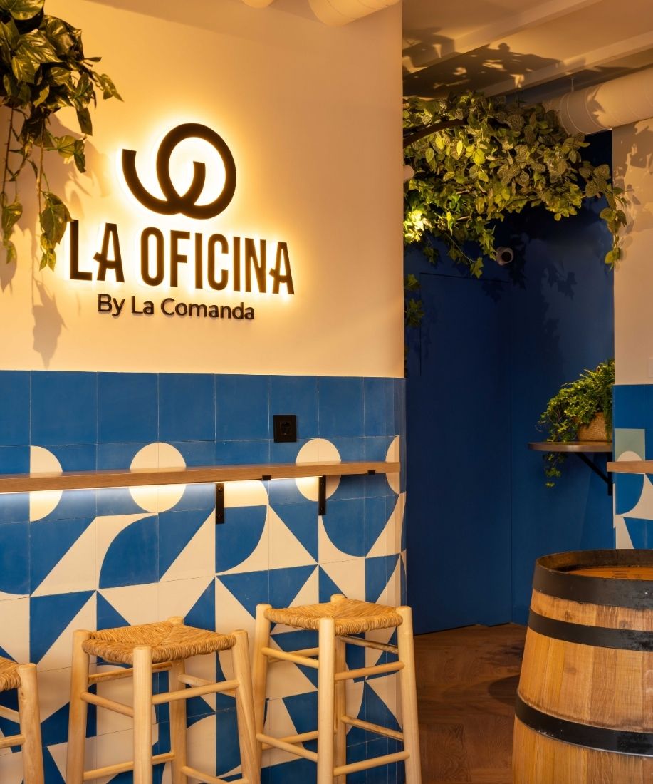 Rótulo luminoso La Oficina by La Comanda sobre pared de azulejos azules y blancos