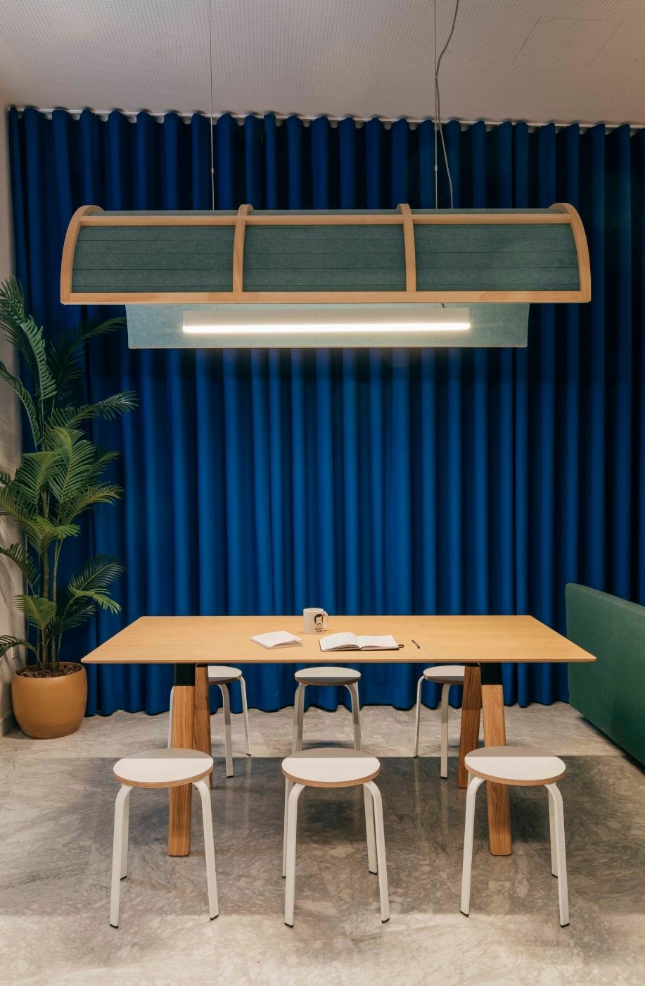 Mesa de trabajo colaborativo con taburetes y cortina azul en las oficinas de Uptodown
