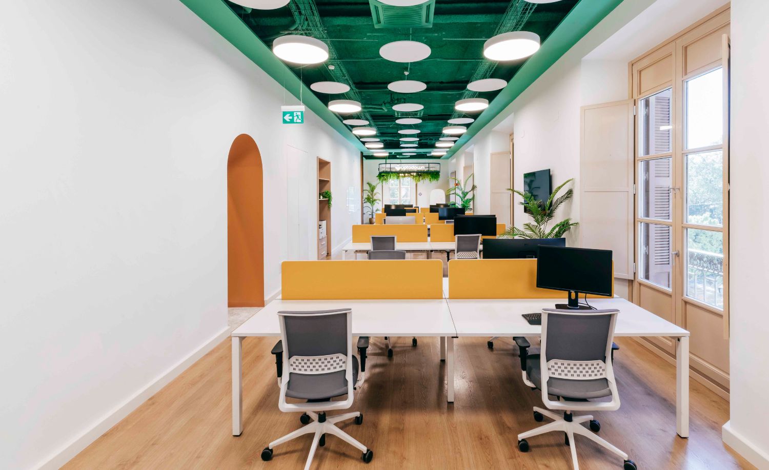 Zona de trabajo con mesas compartidas, techo verde con focos y arco naranja en Uptodown
