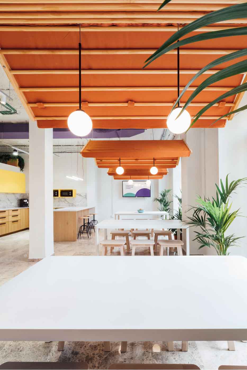 Zona de office con paneles de madera naranja en el techo y mesa blanca en las oficinas de Plytix