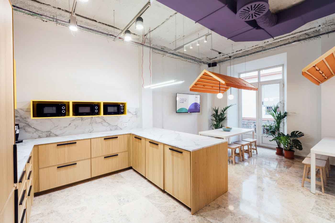 Office con muebles de madera, microondas amarillos y zona de comedor al fondo en las oficinas de Plytix