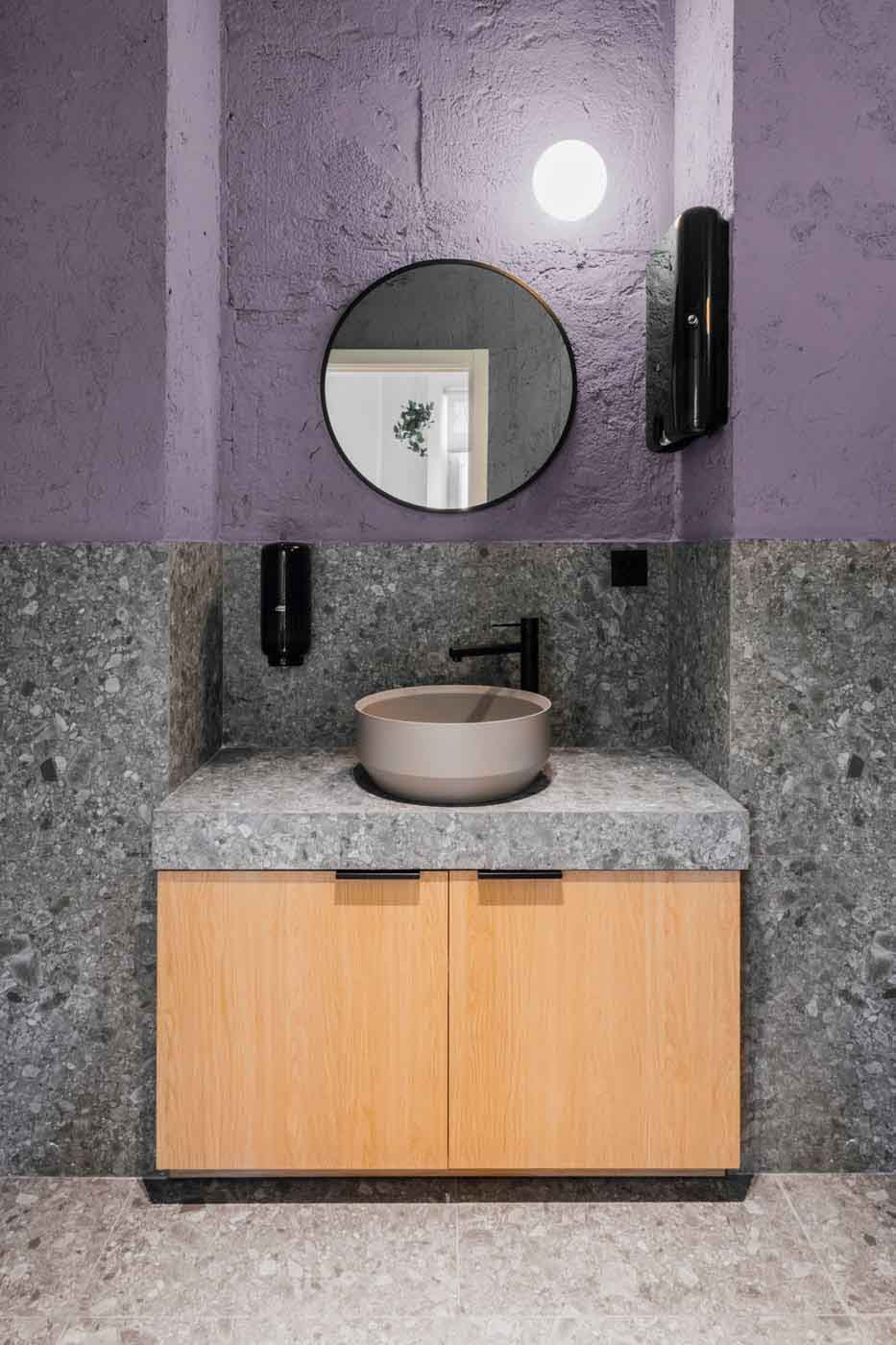 Aseo con lavabo sobre encimera y pared morada en las oficinas de Plytix