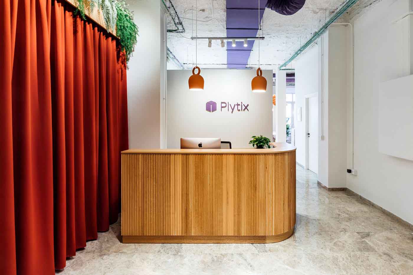 Recepción con mostrador de madera curvo, logotipo de Plytix y cortina roja