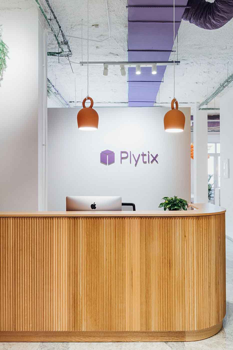 Mostrador de recepción de madera con lámparas colgantes y logotipo de Plytix en la pared
