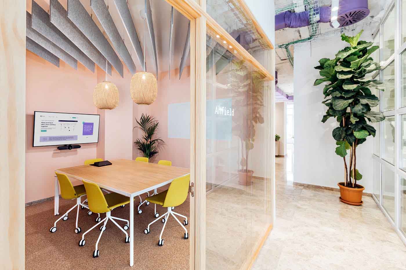 Sala de reuniones con mesa de madera, sillas amarillas y paneles acústicos en las oficinas de Plytix