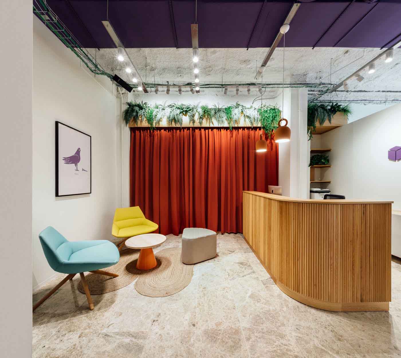 Recepción con mostrador de madera, cortina roja y sillones de colores en las oficinas de Plytix