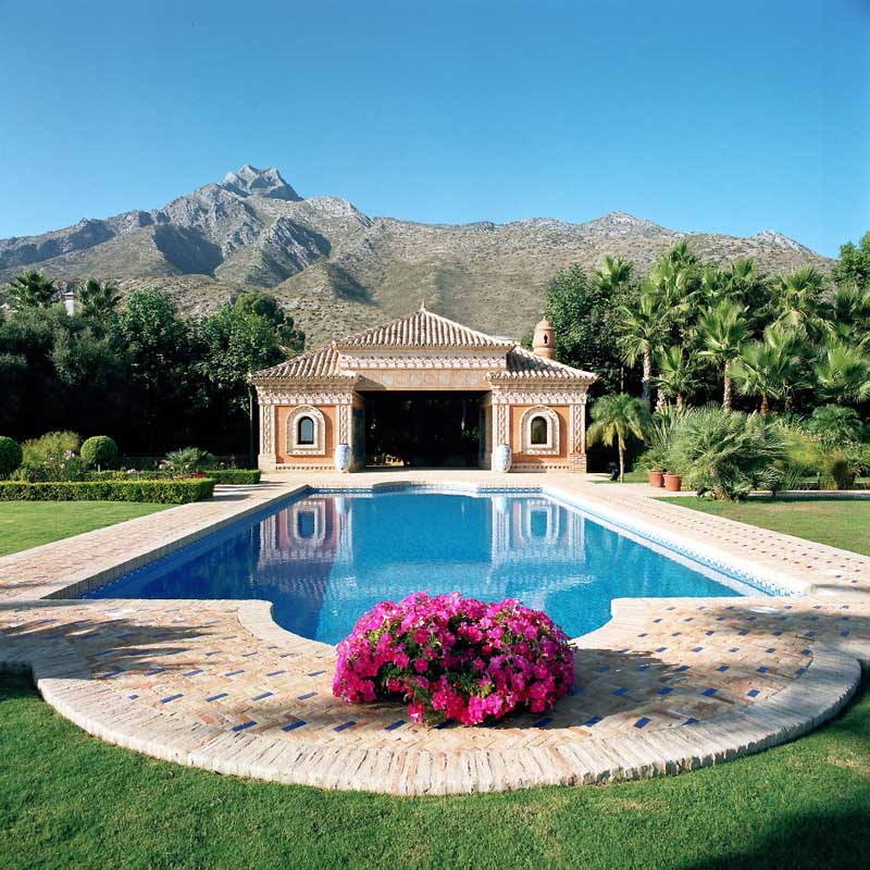 Piscina con macizo de flores y pabellón con la sierra al fondo en Marbella