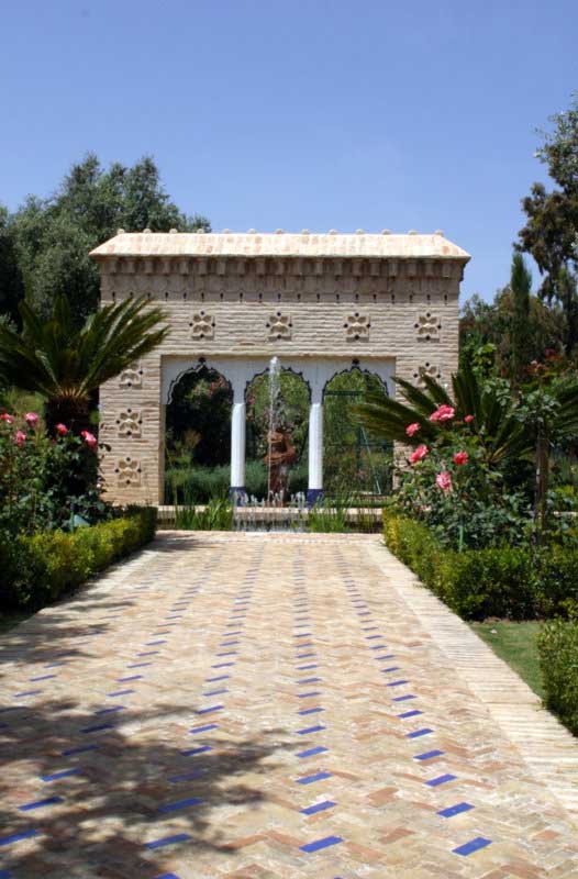 Paseo pavimentado con azulejos hacia un arco ornamental entre jardines en Marbella