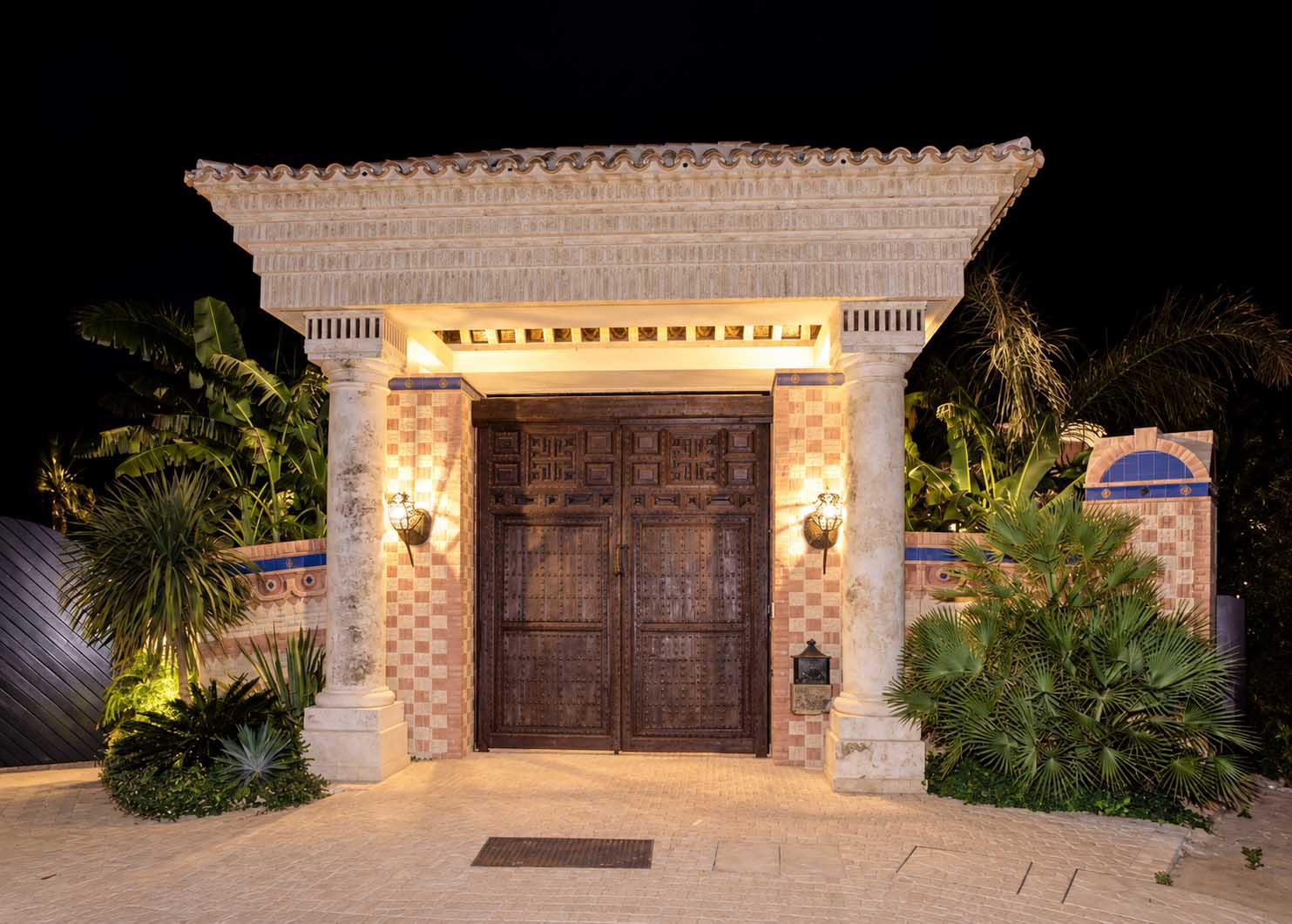 Portada de entrada iluminada de noche con puerta de madera tallada en la villa de Marbella