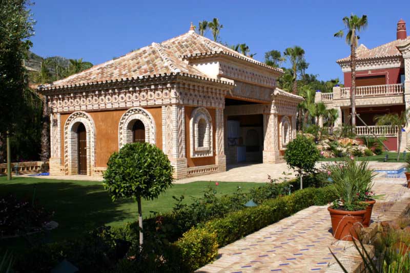Edificación auxiliar de arquitectura tradicional con arcos entre jardines cuidados en Marbella