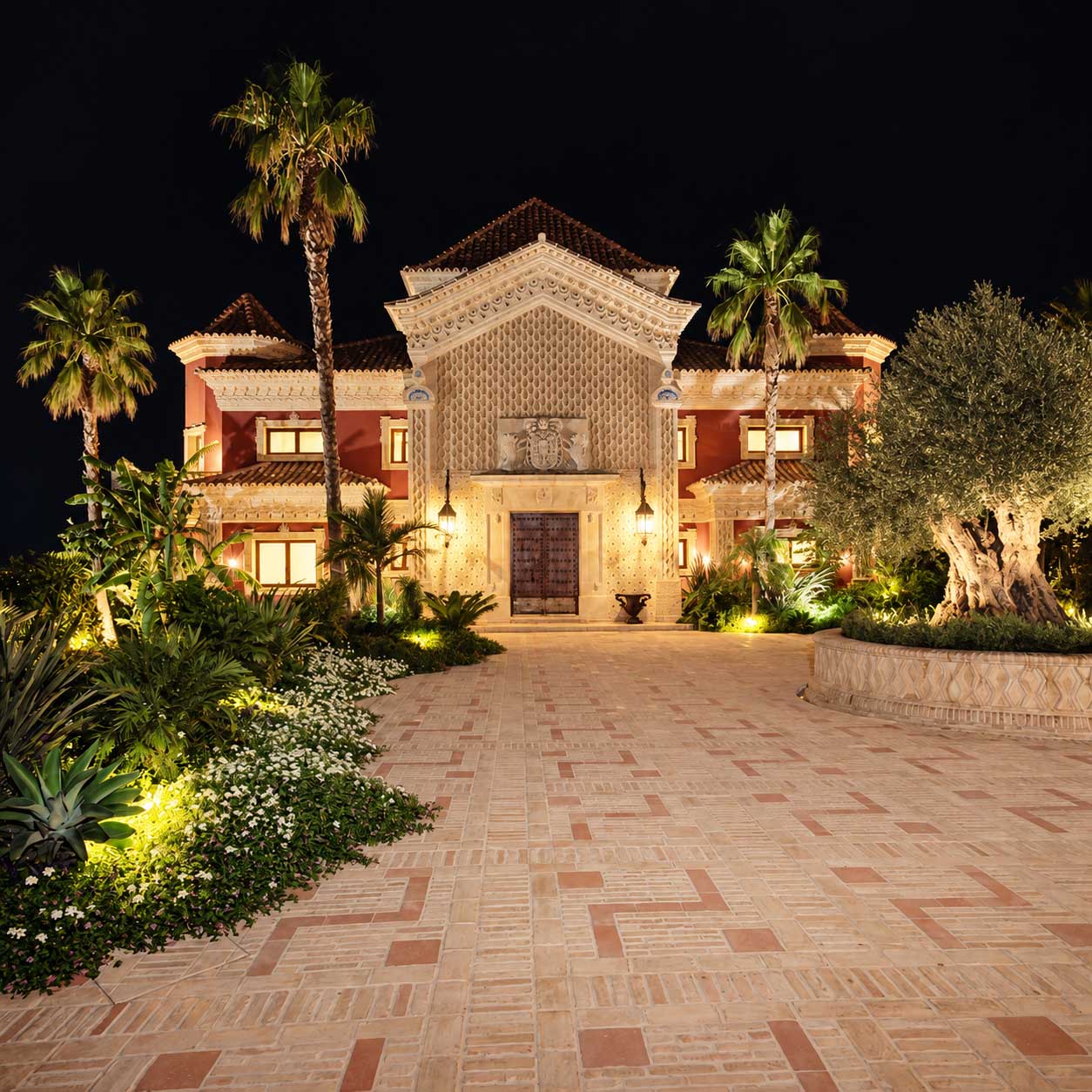 Villa iluminada de noche con patio empedrado y palmeras en Marbella