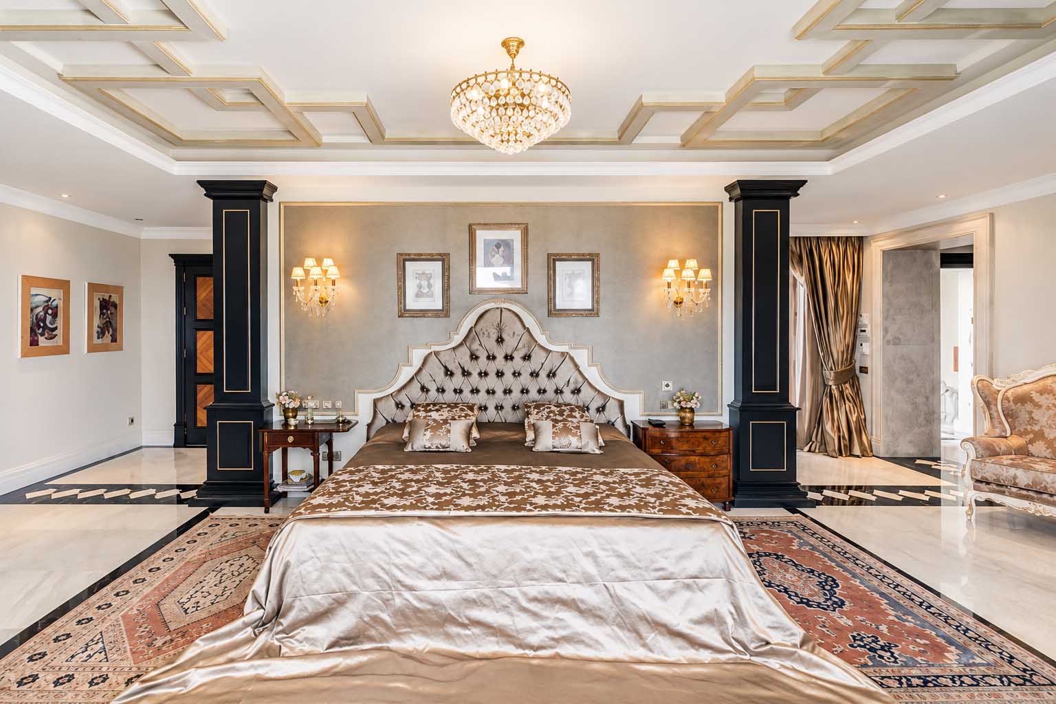 Dormitorio principal con columnas, cama capitoné y techo decorativo en la Villa Alhambra