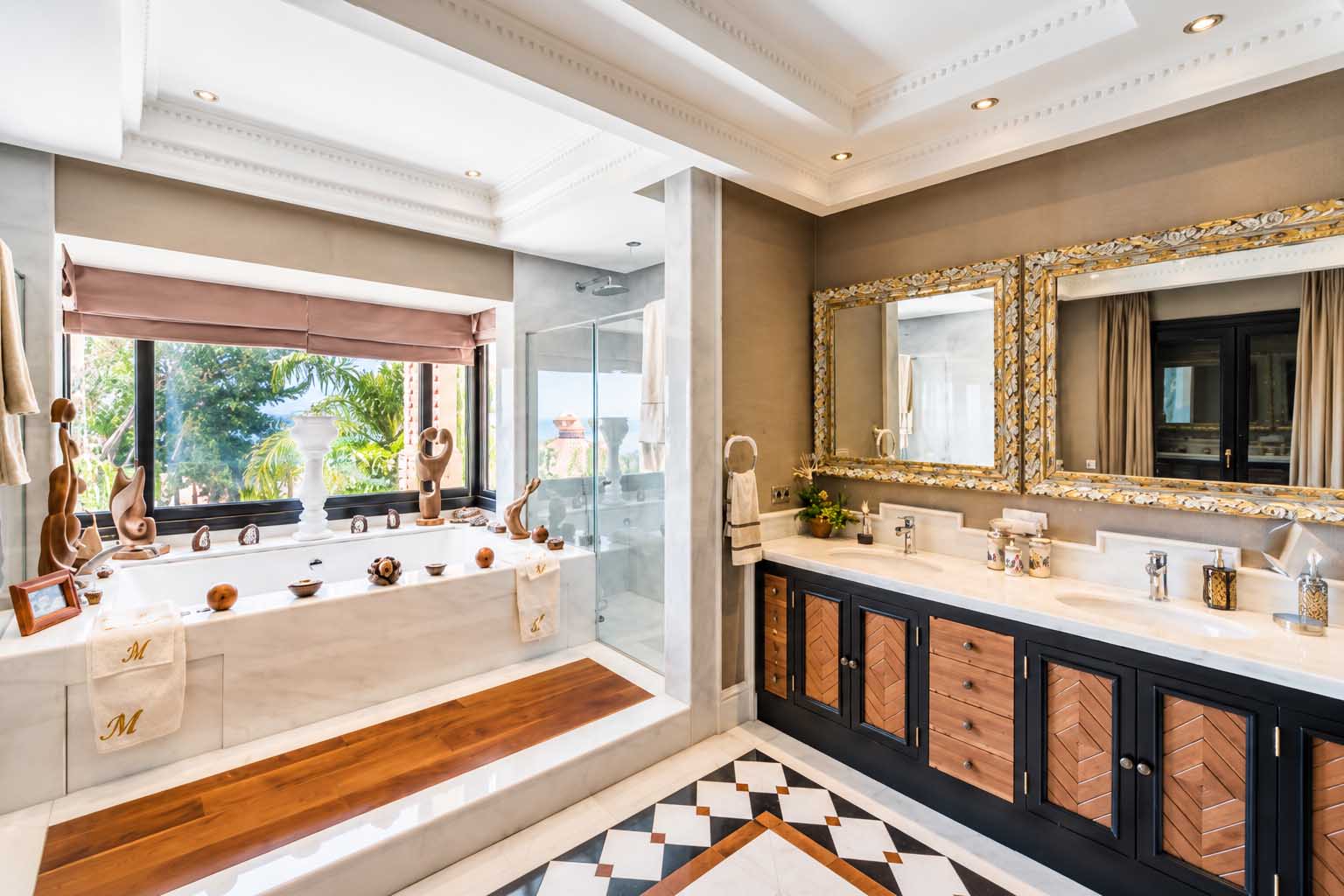 Baño con bañera junto a la ventana y encimera con espejos dorados en la Villa Alhambra