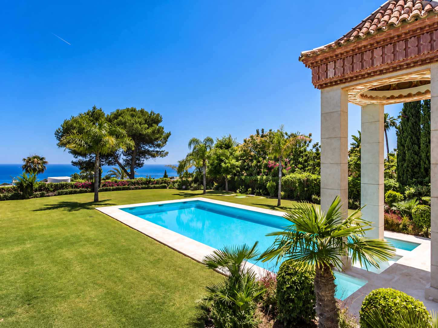 Jardín con piscina, palmeras y pérgola de columnas con vistas al mar en la Villa Alhambra