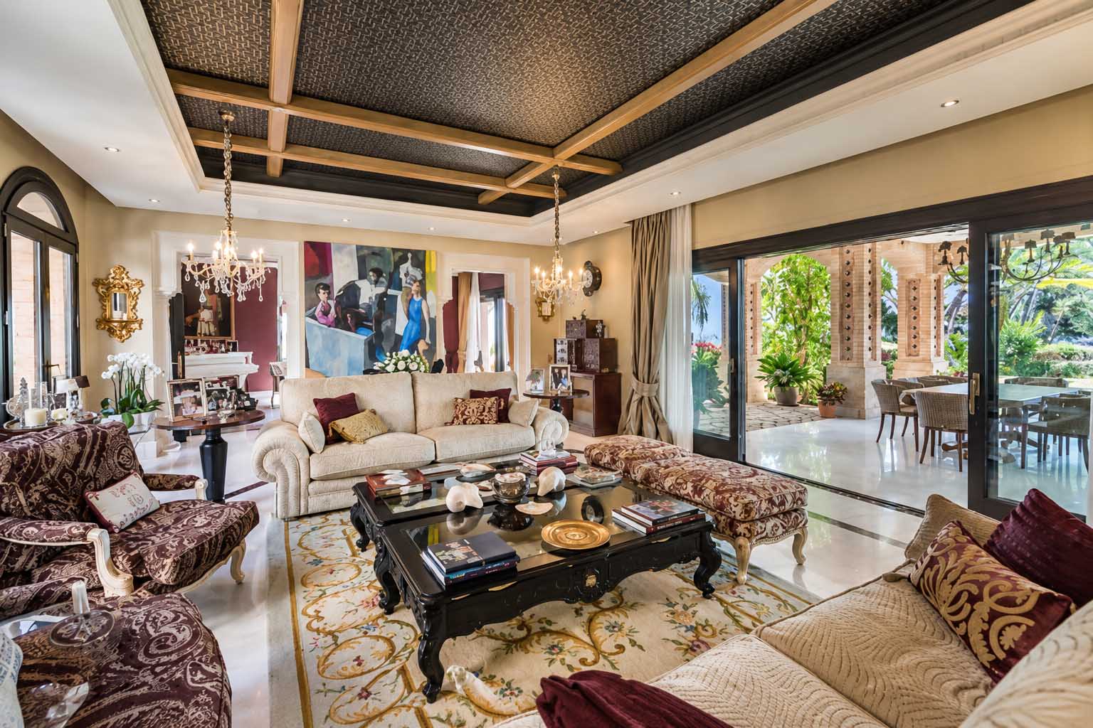 Salón amplio con sofás, techo decorado y salida al jardín en la Villa Alhambra