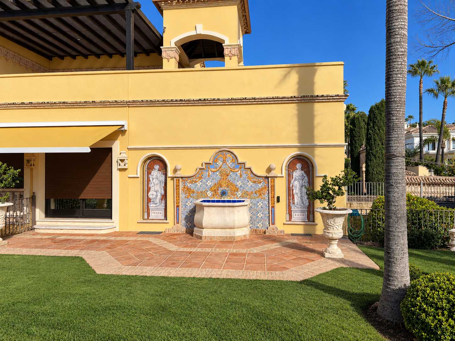 Pabellón de fachada amarilla con fuente de azulejos y hornacinas en el jardín de la Villa Casa Blanca
