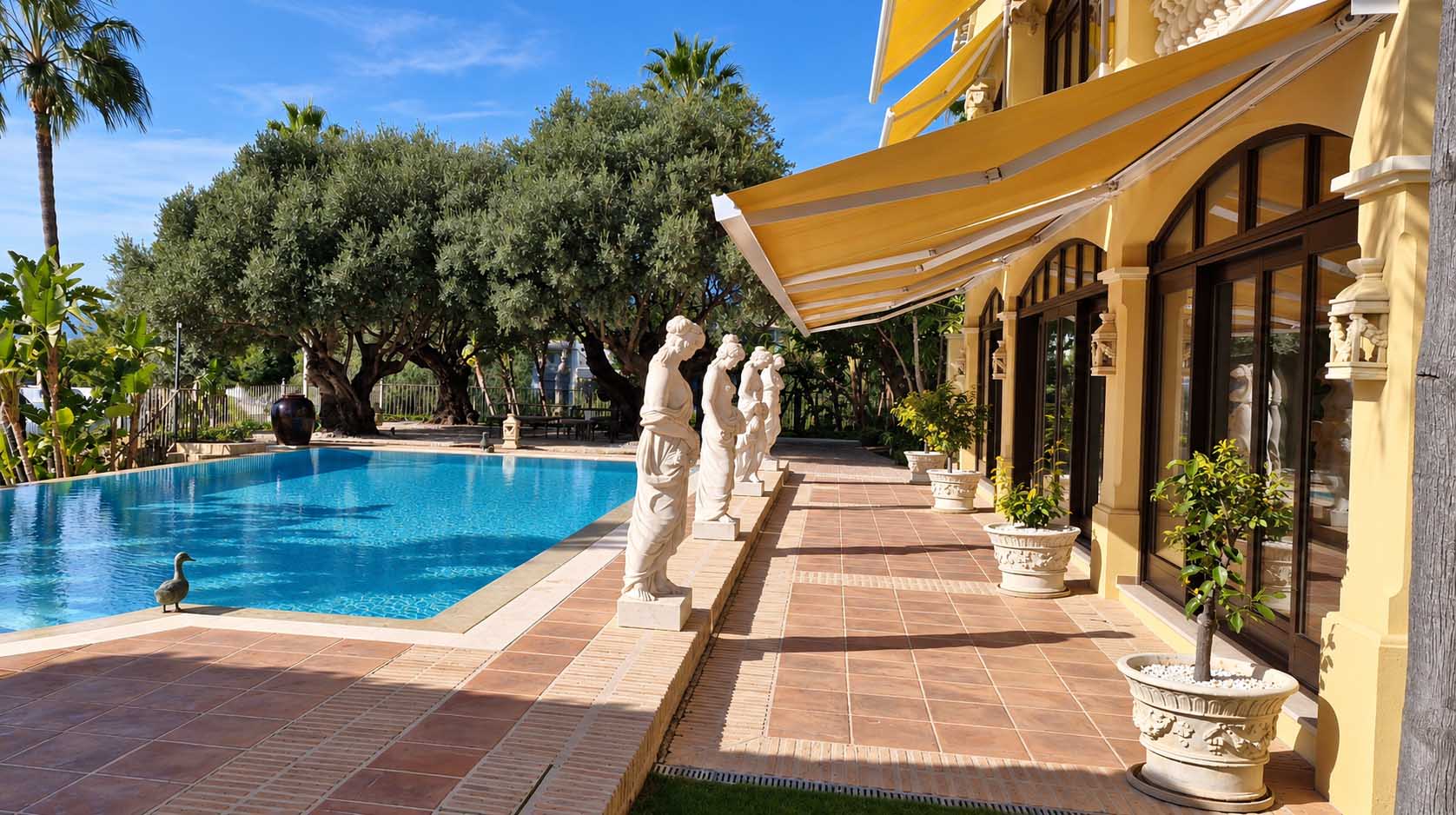 Piscina con esculturas y porche con toldo en la Villa Casa Blanca de Marbella