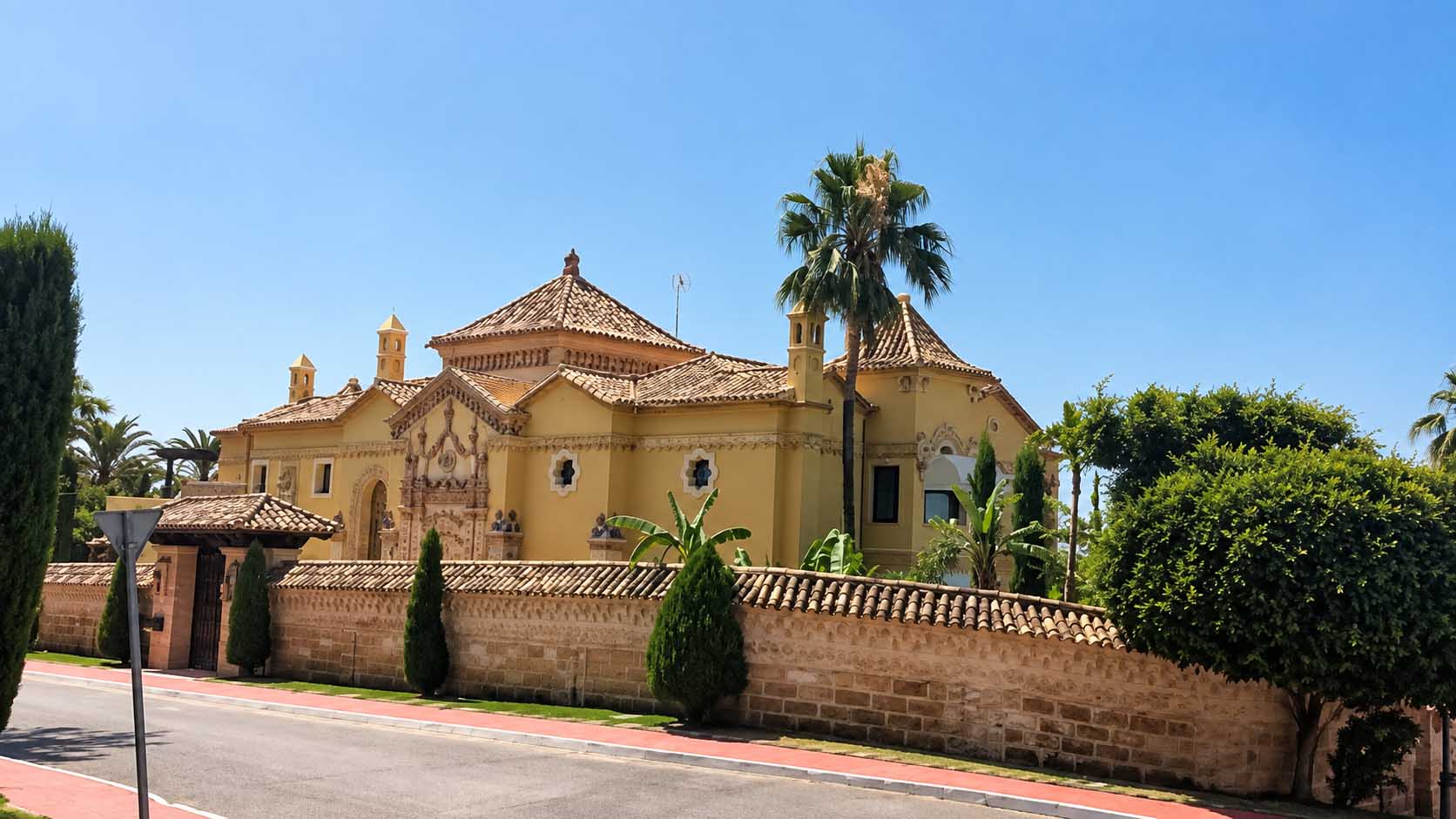 Villa Casa Blanca de fachada ocre tras el muro de ladrillo y la palmera en Marbella