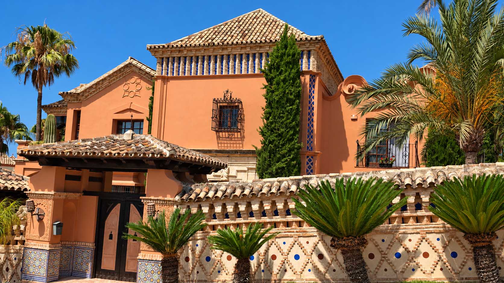 Fachada naranja con teja cerámica, palmeras y cerramiento ornamental en la Costa del Sol