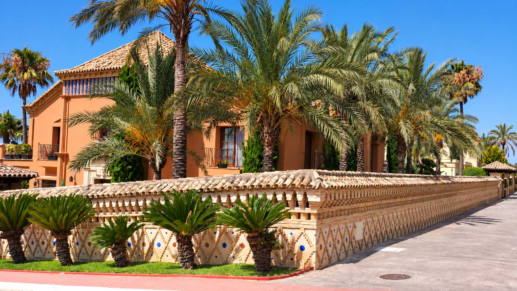 Muro ornamental de ladrillo y cerámica entre palmeras junto a la villa