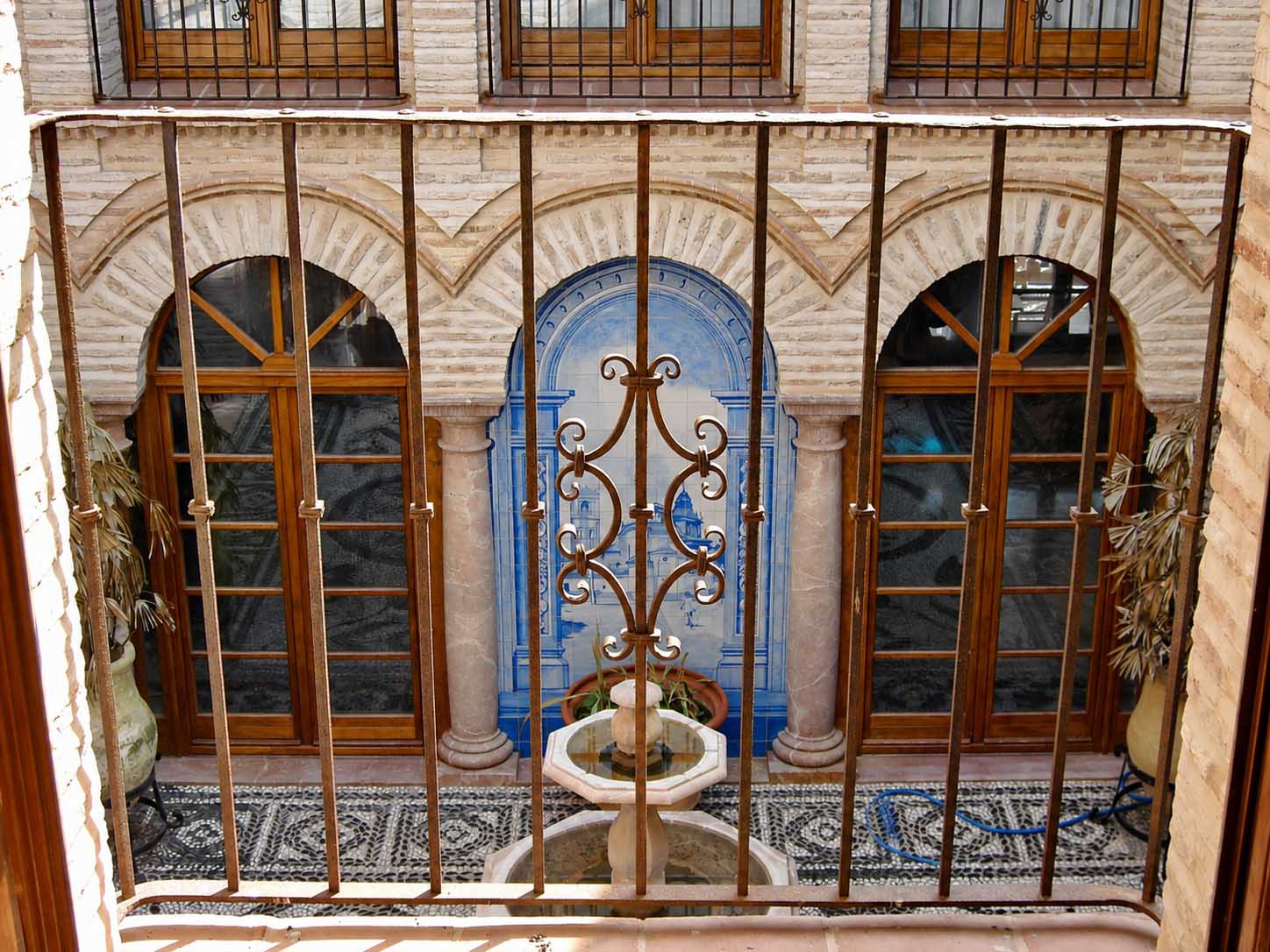 Ventanales con arcos, reja de forja y panel de azulejos en la fachada interior